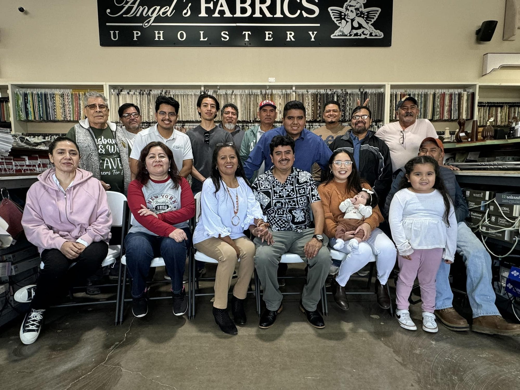 The Angel's Fabrics and Upholstery team and family gathered beneath the shop sign